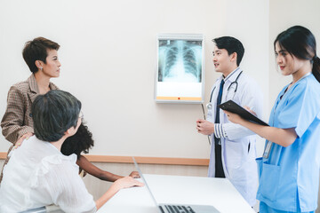 A team of young Asian male doctor and female nurse in lab coat with stethoscope in conversation with patient while writing details and explaining x-ray reports in a clinic or hospital cabin