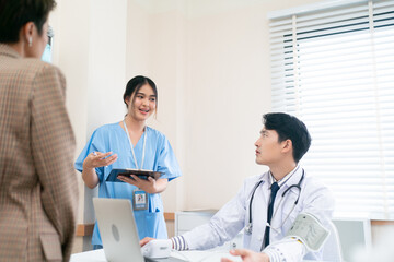 Fototapeta premium Mature female doctor discussing medical report with nurses in hospital hallway. Senior general practitioner discussing patient case status with group of medical staff after surgery. Doctors working.