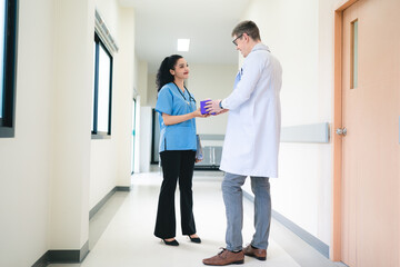 Mature female doctor discussing medical report with nurses in hospital hallway. Senior general practitioner discussing patient case status with group of medical staff after surgery. Doctors working.