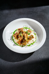 Crunchy eggplant with stracciatella cheese and a drizzle of green sauce on a white plate