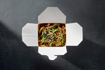 Takeout concept with udon noodles, shrimps, and seafood, garnished with sesame and green onion in a...