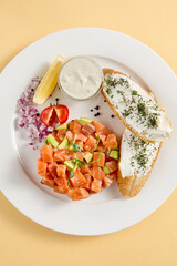 Salmon tartare with avocado on toasted bread with cream cheese, top view on a white plate with copy space. Ideal for restaurant menus and recipe websites