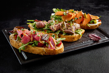 Gourmet bruschetta set with salmon, roast beef, and tuna on a black plate, side angle view