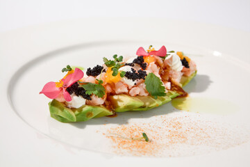 Gourmet avocado with shrimp tartare, mango, cream cheese, and black caviar on a pristine white plate