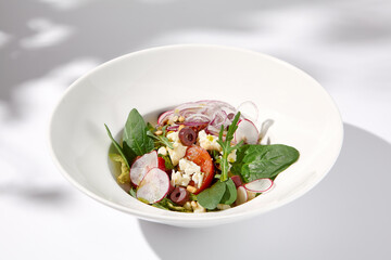 Greek salad with feta cheese, olives, and crisp vegetables, cast with shadows on a white background