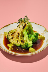 Broccoli steak in ponzu sauce on a white plate with golden trim, close-up against a pink background
