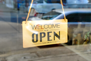 welcome we are open please come in sign on the glass door of the coffee shop