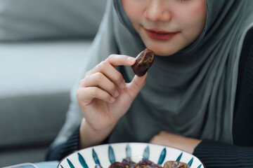 Muslim woman in hijab eating dates fruit in a comfortable home. Clouse up shot.