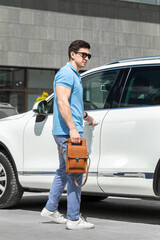 Young man with brown leather bag standing near the car