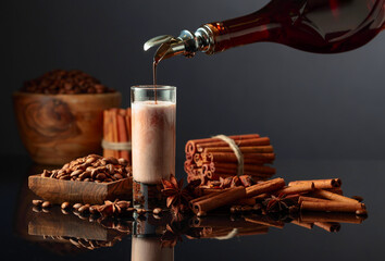 Coffee liquor is poured from a bottle into a glass with cream.