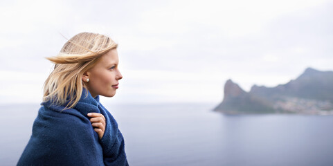Thinking, ocean and woman with blanket in nature for adventure on holiday, vacation and weekend outdoors. Mountain, travel and person by seaside for relaxing, happiness and peace in countryside