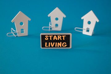 Start living symbol. Concept words Start living on black blackboard near miniature houses. Beautiful blue background. Business and Start living concept. Copy space.