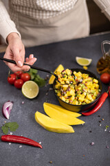 Freshly made mango salsa in a black ceramic bowl on a table with ingredients