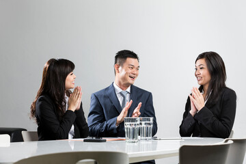 Happy Chinese business people applauding in a meeting.