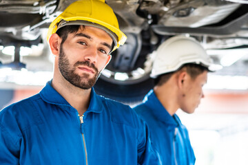 Automotive mechanic man in uniform with assistant working at auto garage shop. Car repairing and...