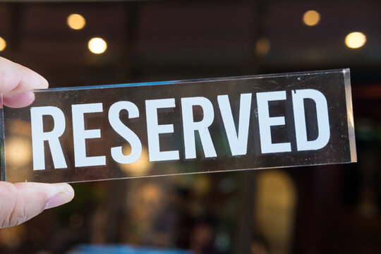 Reserved sign on hand with light bokeh background. Reserved sign for dinner