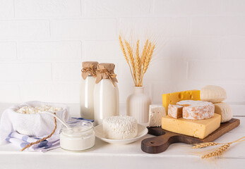 Delicious fresh dairy products for Shavuot on a wooden cutting board and a white table. A vase with...