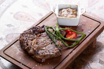 Fresh cooked medium rare steak served with pepper and tomatoes on wooden board at restaurant, healthy protein dinner