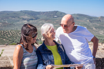 Smiling group of mature seniors visiting a historic castle in Andalusia, Spain, looking at the map and landscape from above. Travel and tourism concept, olive tree crops in the background