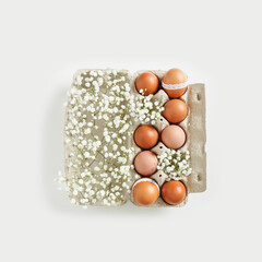 Brown Easter eggs decorated lace and white gypsophila flowers in carton on white background. Easter celebration concept. Top view photo of festive food of dyed chicken egg, minimal style, copyspace