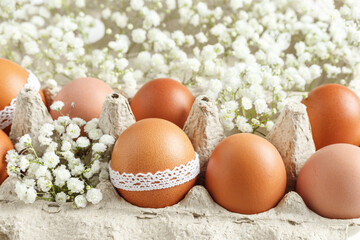 Brown Easter eggs decorated lace and white gypsophila flowers in carton on white background. Easter celebration concept. Top view photo with festive food of organic painted chicken egg