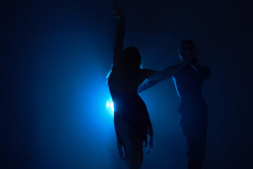 Classical Ballroom or salsa dancers dance in dark smoky studio, with backlight. isolated. Couple of slim slender man and woman in suits. The grace, artist, movement, action and motion concept.