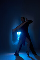 Male and female engaged in ballroom, standard, sport dance, latin and salsa couple dancers in dark...
