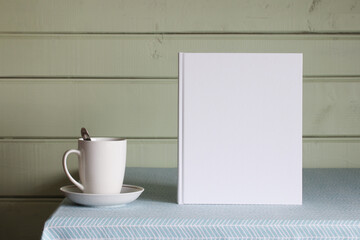 a book with an empty white cover. mockup album, copy space. a book and a mug on the table in the cottage.