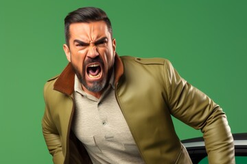 Fototapeta premium 41-year-old Hispanic man, his brows furrowed in rage, gesturing aggressively, fueled by road rage during a traffic jam, on a solid pastel green background
