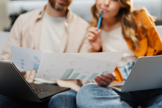 Attractive Busy Man And Woman, Freelancers Working At Home, Holding Documents, Graphs, Using Laptop