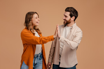 Attractive couple, man and woman giving each other high five standing isolated on beige background