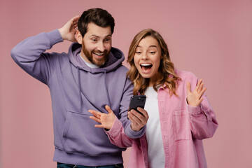 Excited, smiling woman and man wearing stylish colorful clothes, holding mobile phone, win money