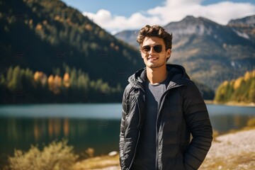 A male tourist in front of a scenic mountain lake with lush green surroundings and cloudy sky