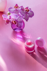 lip balm with orchid in glass vase on pink background