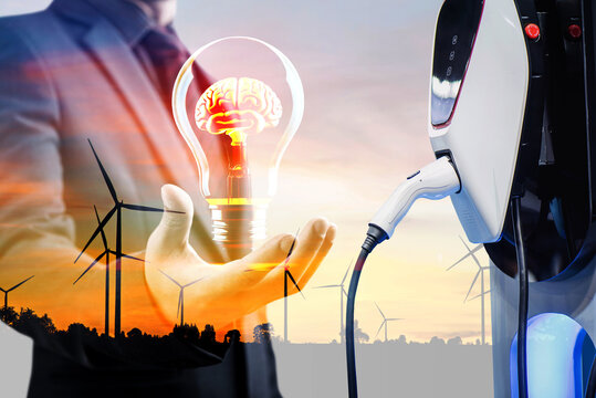 double exposure of businessman hold lightbulb and silhouette of wind turbine at sunset with electric car battery charger station. Green energy for new innovative EV Electrical vehicle concept.