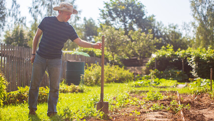 The farmer stands with a shovel in the garden. Preparing the soil for planting vegetables. Gardening concept. Agricultural work on the plantation