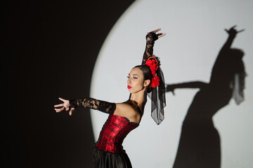 Woman dancing on black background under spotlights. Spanish dancer in red-black dress dancing elements of passionate flamenco.
