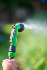 Farmer's hand with garden hose and gun nozzle watering vegetable plants in summer. Gardening concept. Agriculture plants growing in bed row