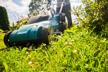 Lawn mower in motion on green grass in garden or backyard. Machine for cutting lawns. Gardening care tools and equipment. Process of lawn trimming