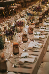 
Detalle de la decoración vintage de una mesa preparada para celebrar una cena de boda. Destacan la cristalería rosa y los adornos florales. La cristalería y vajilla es transparente.