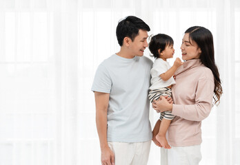 cheerful father and mother holding and talking with toddler baby on white window background. happy family