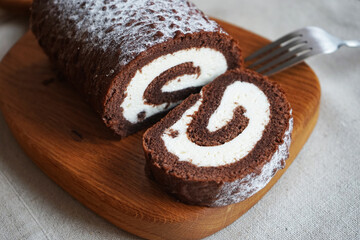Chocolate sponge roll with vanilla cream on a wooden board on a light background