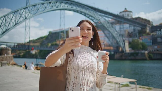 Cheerful blogger holding smartphone recording video at river promenade closeup