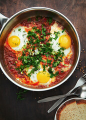 Tasty and healthy shakshuka, Middle Eastern omelet in a frying pan. Delicious scrambled eggs cooked in spicy tomato pepper sauce on rough wooden table. Top view