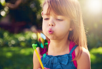 Young girl, backyard and blowing pinwheel, garden and enjoying freedom of outside and fun. Pretty...