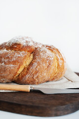 Fresh bread on a wooden board and linen tablecloth next to a knife on a white background