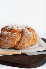 Fresh bread on a wooden board and linen tablecloth next to a knife on a white background