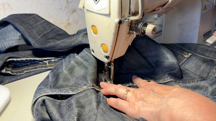 Untitled Sewing work. Stitching a hole in jeans with a sewing machine. Seamstress sews with jeans cloth. Darning jeans on a sewing machine. Seamstress sews on a sewing machine. Tailoring. - obrazy, fototapety, plakaty