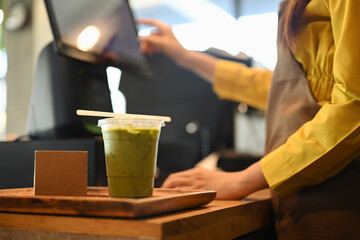 Iced matcha latte in take away cup with paper straw on counter near the cashier in modern cafe