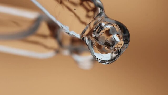 Glass dropper with gel serum for face, close-up, beige background.